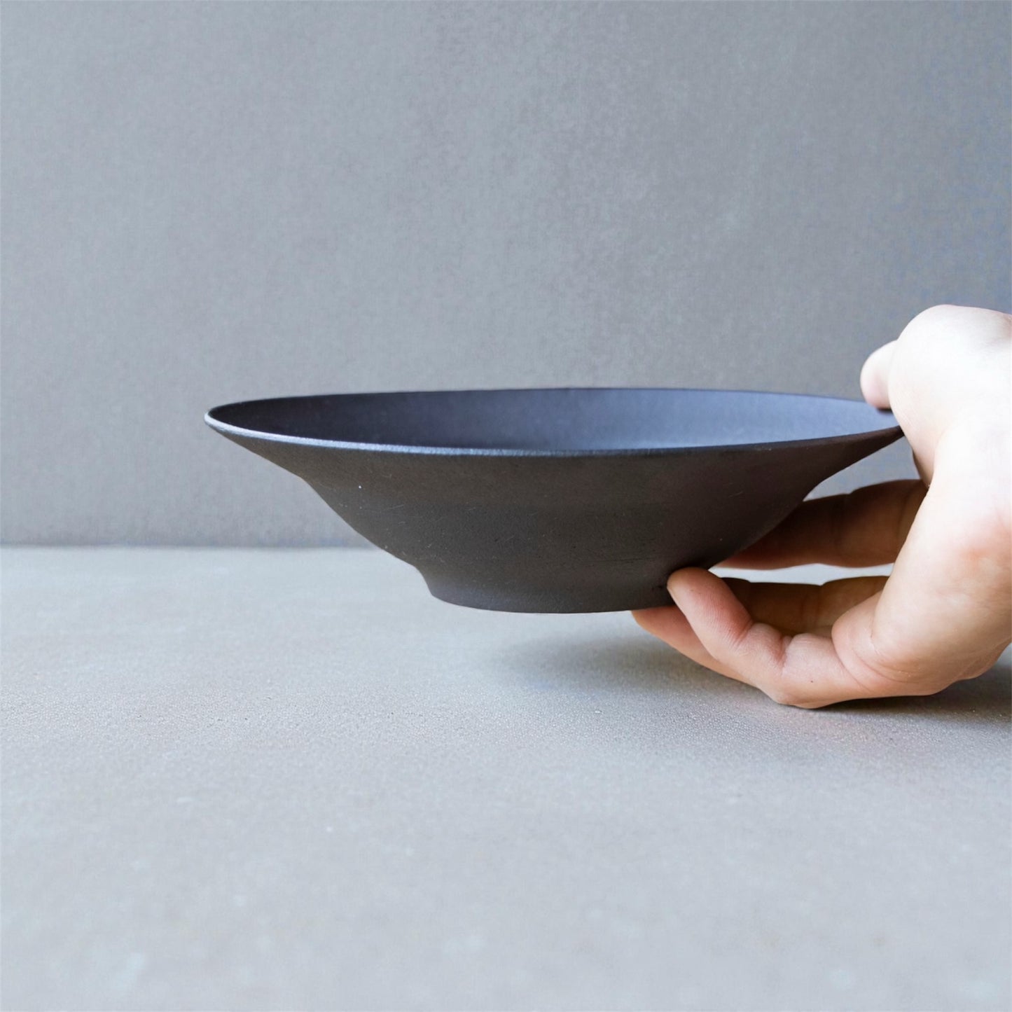 Hand holding a black ceramic bowl against a gray background