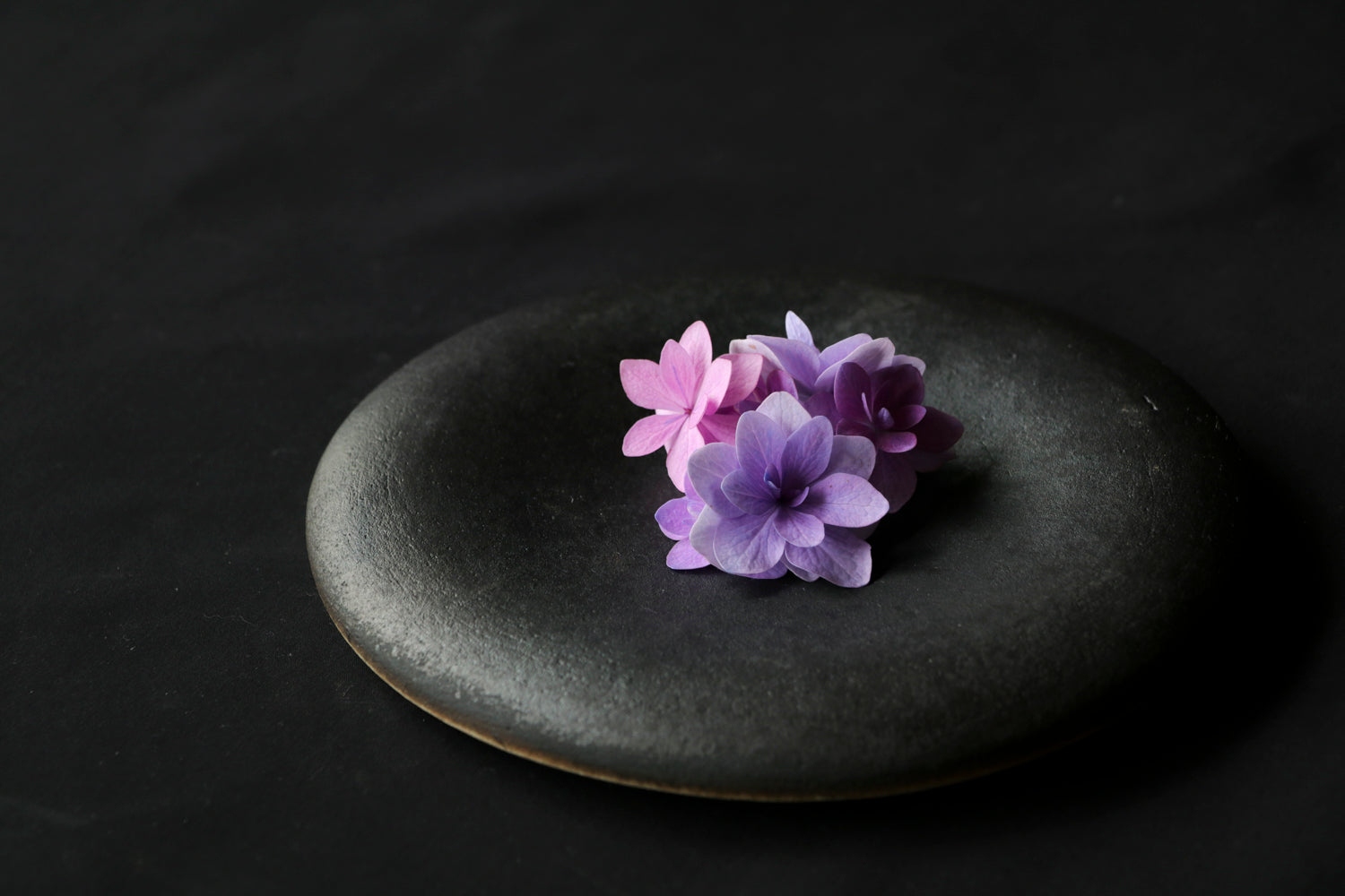 black ceramic round plate that curves in with purple and pink flowers on top