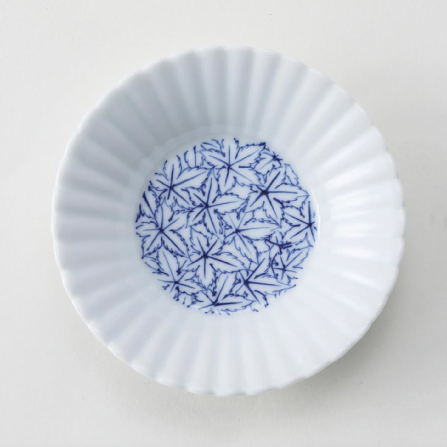 White ceramic fluted plate with blue maple leaves pattern on a light gray background