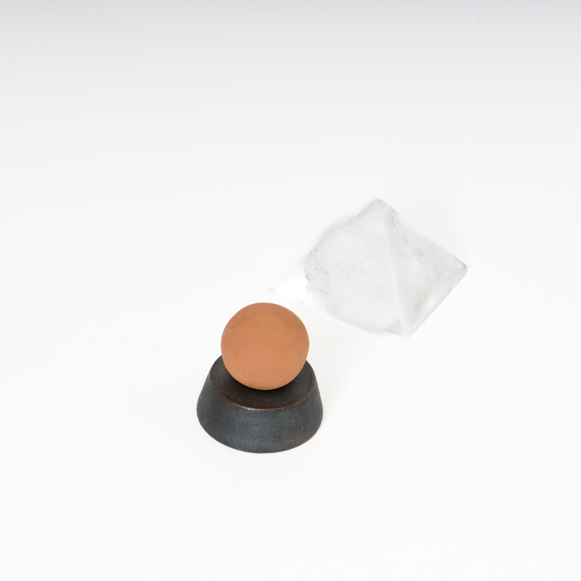 round terracotta ceramic sphere atop a black ceramic circular trapezoid base 