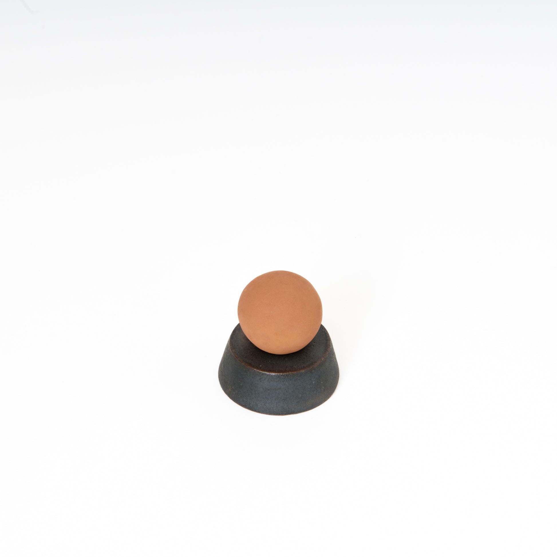 round terracotta ceramic sphere atop a black ceramic circular trapezoid base 