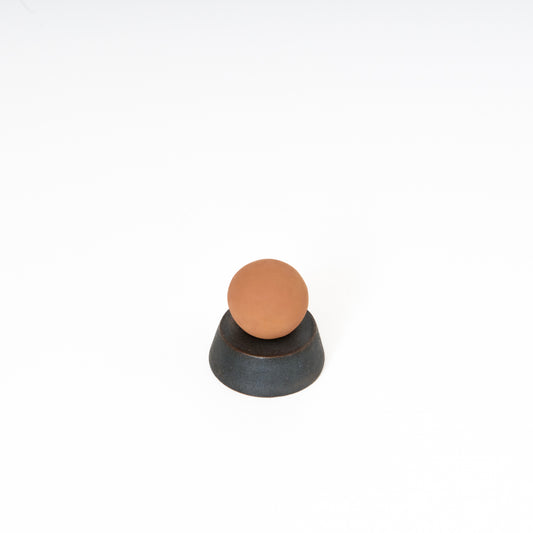 round terracotta ceramic sphere atop a black ceramic circular trapezoid base 