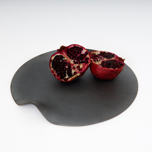 pomegranate cut open in half on a black round ceramic plate with one built in handle 