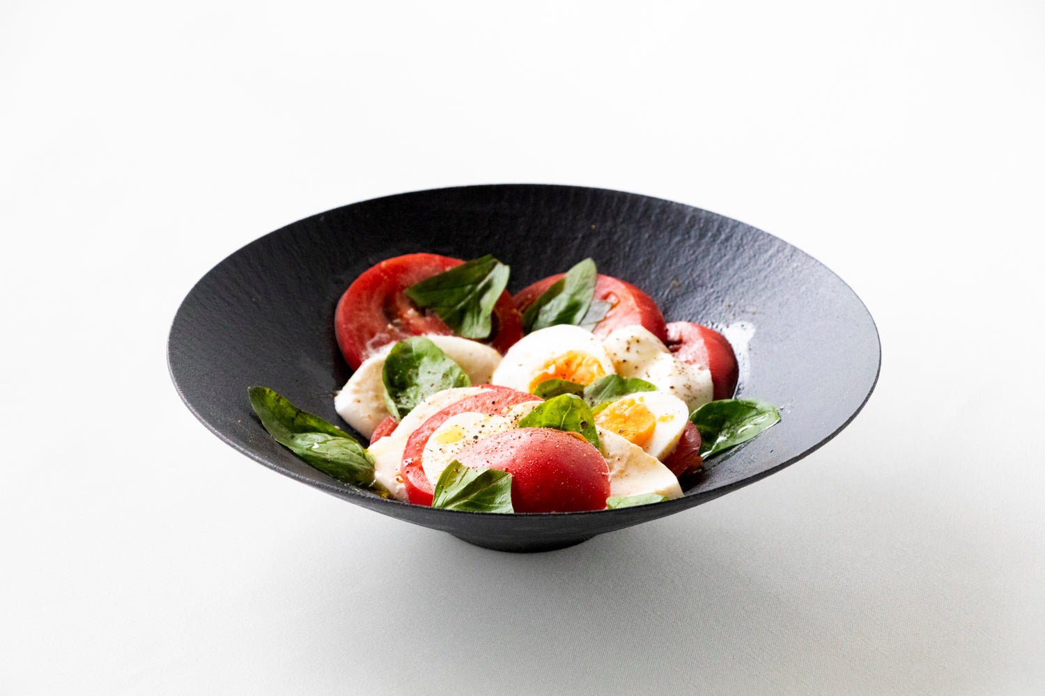 tomato, basil, and egg salad in black ceramic wide bowl 